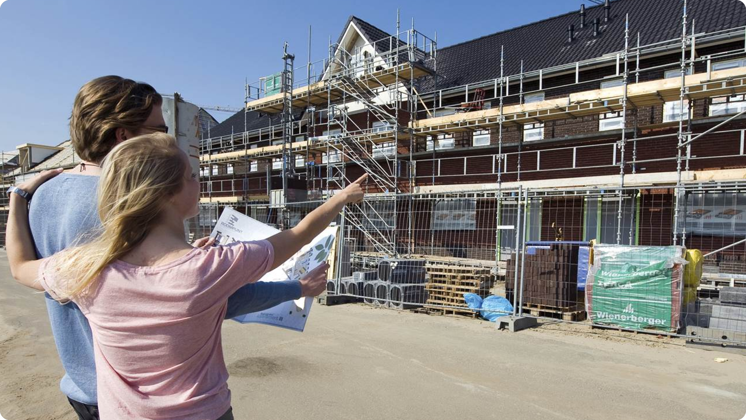 Een stel omarmt elkaar en kijkt naar een nieuwbouwwijk in aanbouw